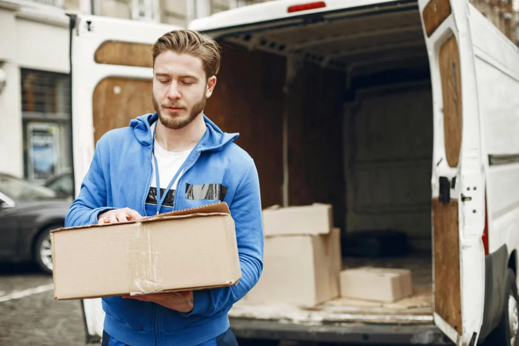 Courier holding a cardboard box beside a delivery van during a commercial drop-off.