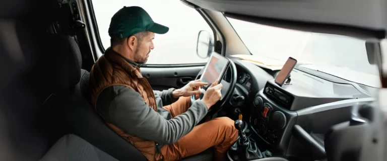 ruck driver inside cabin using a digital tablet for navigation or fleet communication while parked.