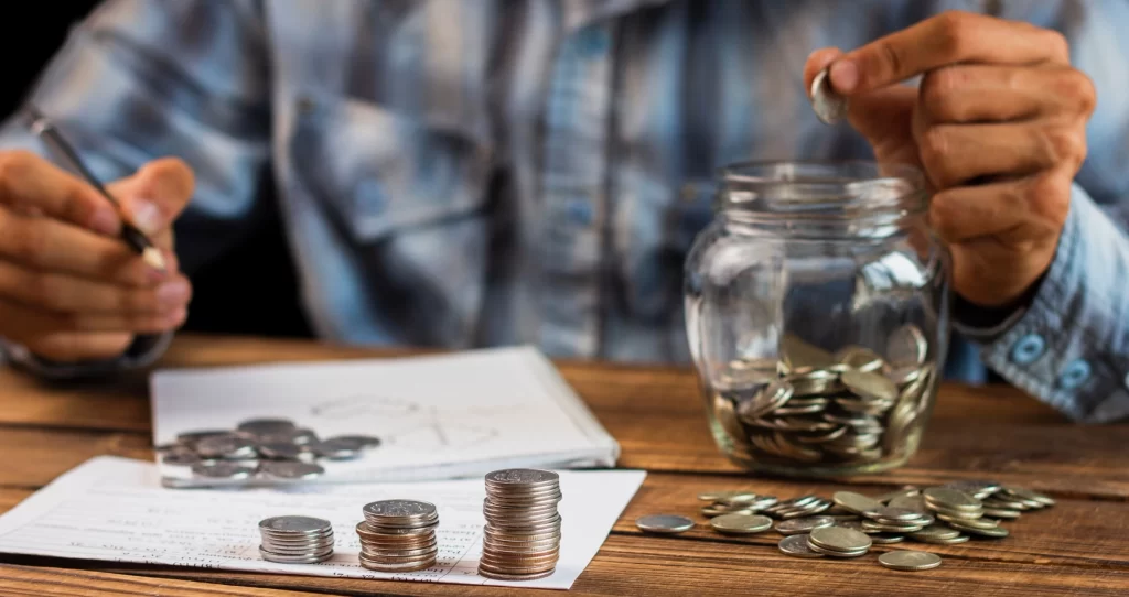 Person counting and organizing coins into stacks while tracking expenses in a notebook—concept of personal finance, budgeting, and saving money.