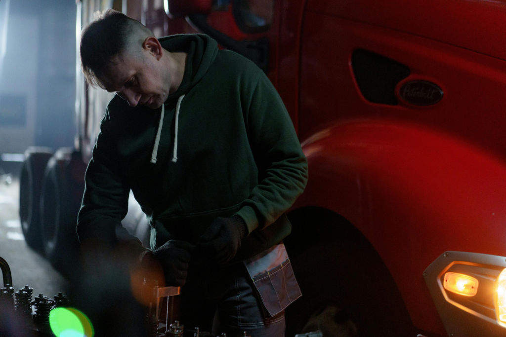 Fleet maintenance technician inspecting engine components next to a red semi-truck, highlighting the importance of vehicle diagnostics in smart fleet software management.