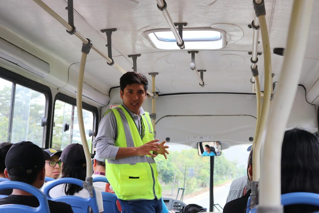 Safety officer giving a passenger briefing inside a company transport bus as part of fleet servicing and compliance.