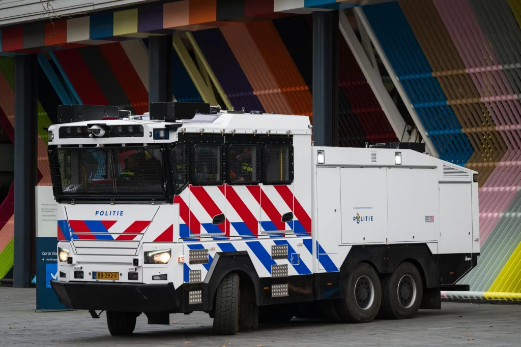 Armored Dutch police water cannon truck parked near a colorful building, used for public safety and crowd control.