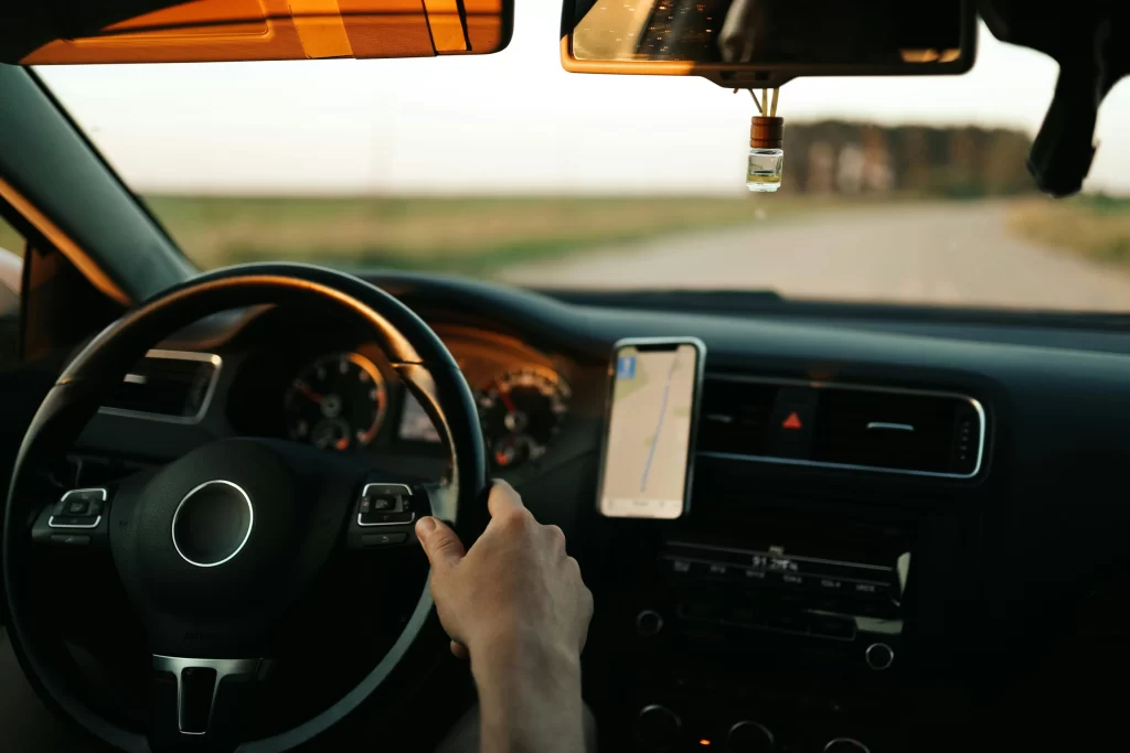 Driver using a smartphone mounted on the dashboard for GPS navigation while driving on an open road.