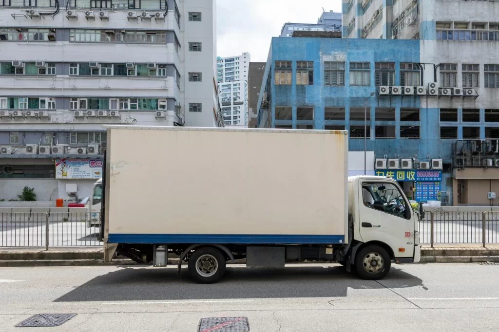 Side view of a white delivery box truck driving through a city, highlighting the importance of last-mile delivery tracking for customer satisfaction.