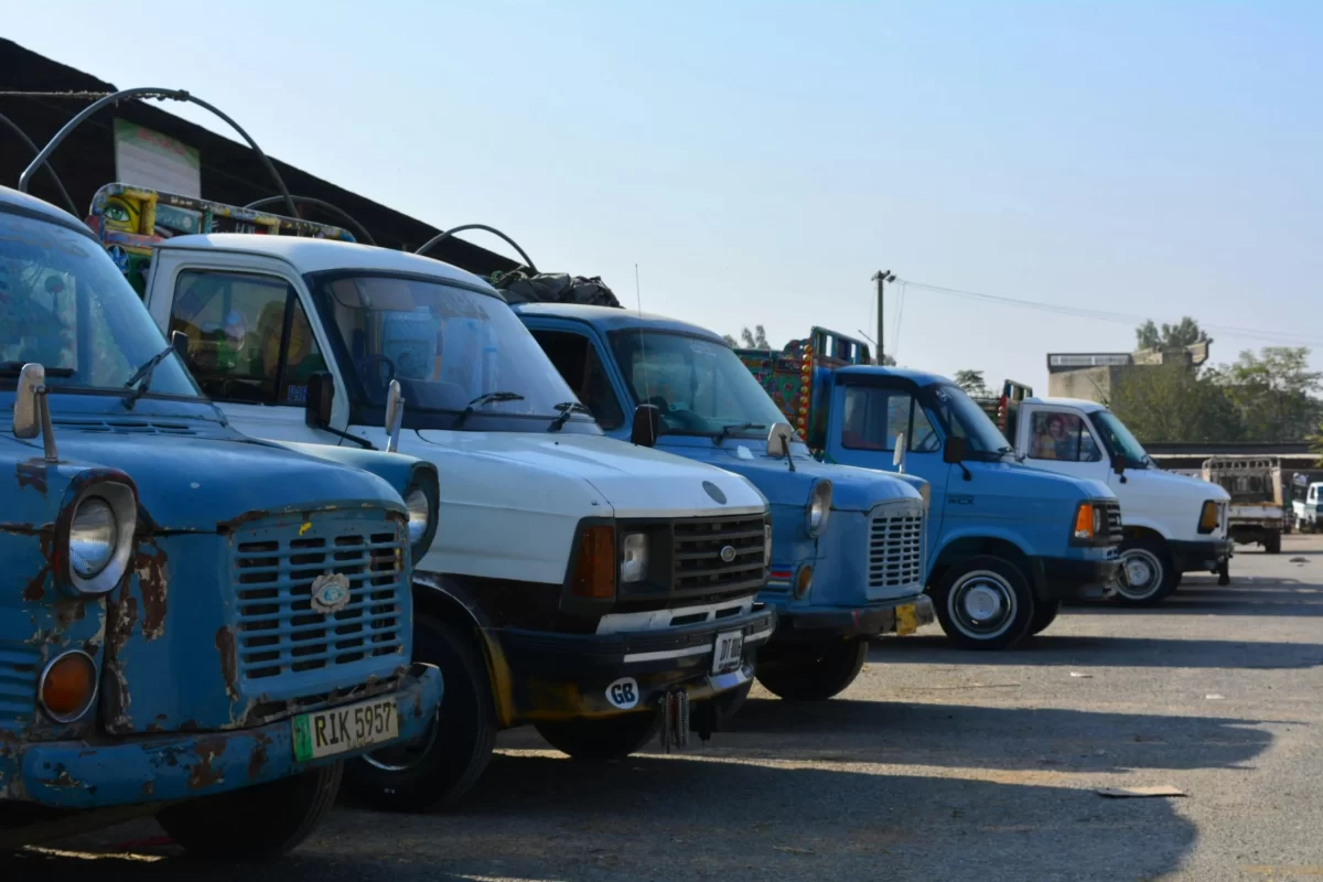 Line of old delivery and transport trucks parked outdoors, showing various models and worn vehicle conditions.