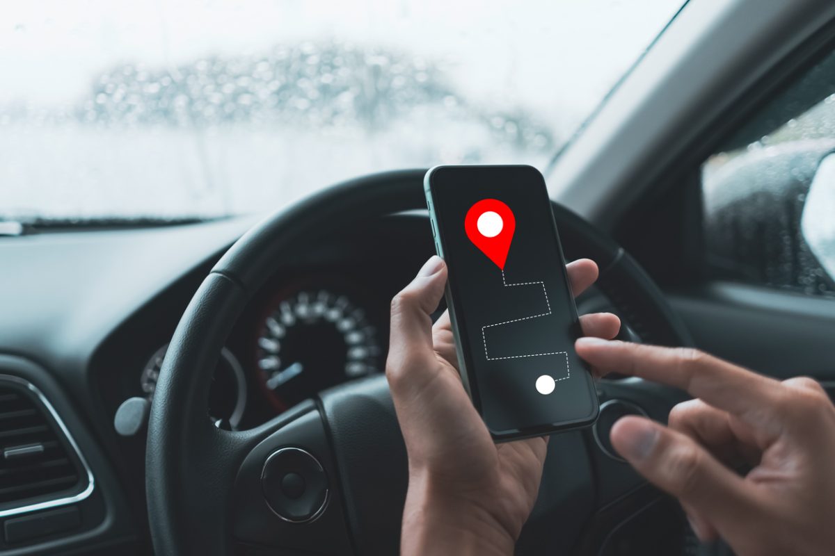 Man hand holding smart phone and searching destination with gps icon navigator map in car and rainy day. Technology lifestyle and transportation concept. Vintage tone filter effect color style.