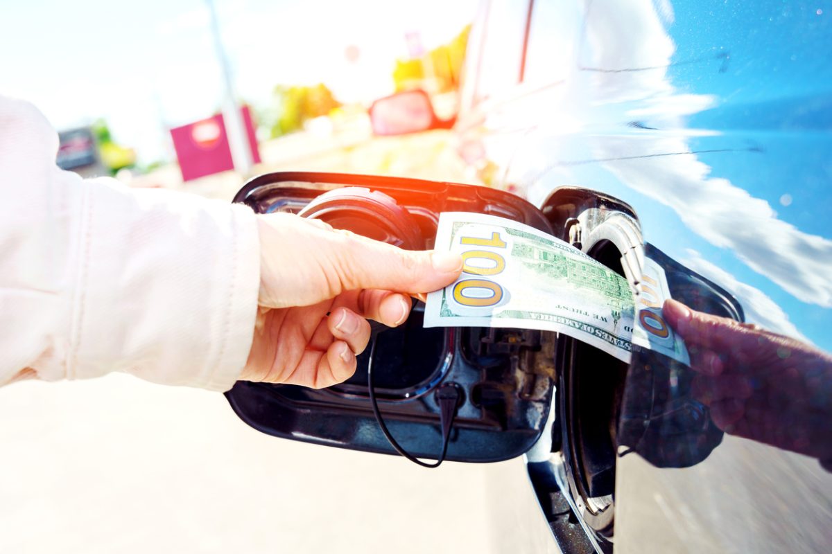 Expensive fuel concept. Rise in fuel price. Hand inserting a hundred dollar bill into the gas tank flap of a car.